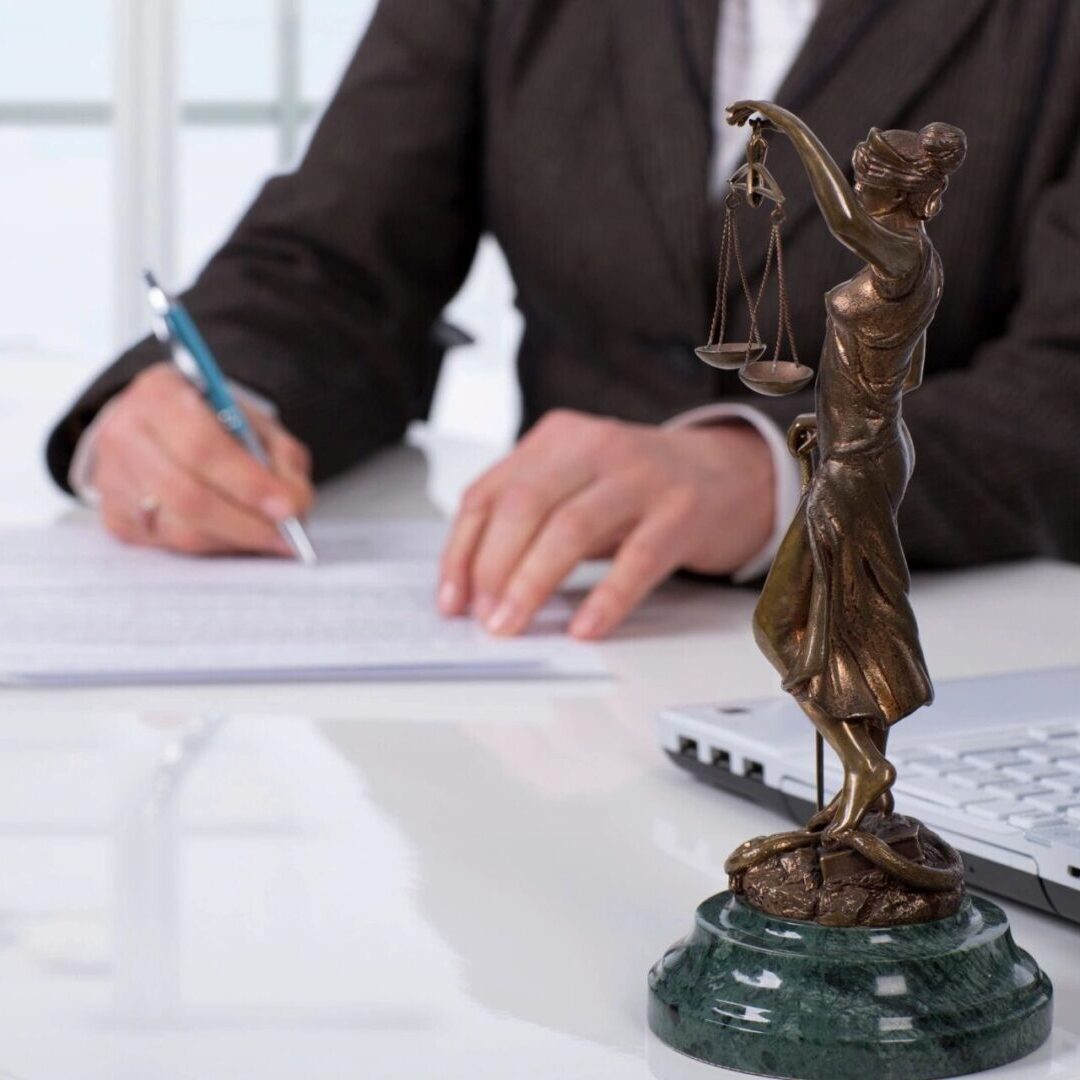 A person writing on paper next to a statue of justice.